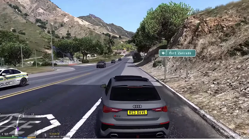 A screenshot from Kasi Vibes latest version in which a grey Audi is driving on a road with a sign pointing to Fort Zenkudo, surrounded by hills and trees. A police car is visible on the side of the road.