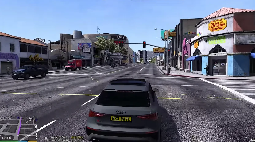 A portrayal of South African culture by a grey Audi car driving on a sunny city street in Los Santos, featuring surrounding commercial buildings, shops, traffic lights, and a mini-map UI.