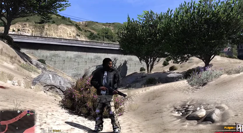 A character from GTA SA Mzansi Kasi Vibes is standing in a sandy area with bushes and trees, holding a weapon, near a concrete structure.