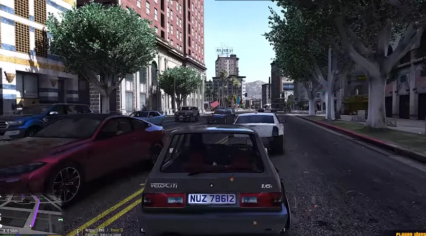 A grey VeloCiTi 1.6i hatchback, depicting tsotsi lifestyle, is driving on a city street in Los Santos, surrounded by other cars, tall buildings, and trees under a clear blue sky.